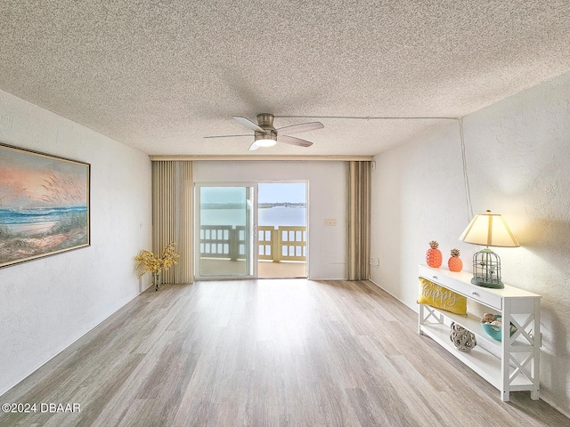 spare room with a textured ceiling, hardwood / wood-style flooring, ceiling fan, and a water view