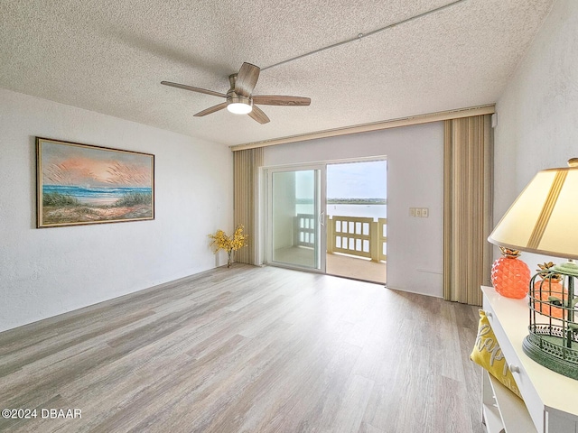 spare room with ceiling fan, a water view, a textured ceiling, and light hardwood / wood-style flooring