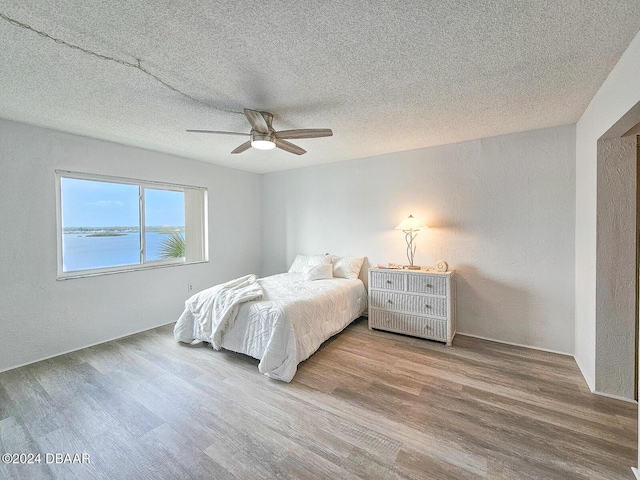 bedroom with a textured ceiling, a water view, and hardwood / wood-style flooring