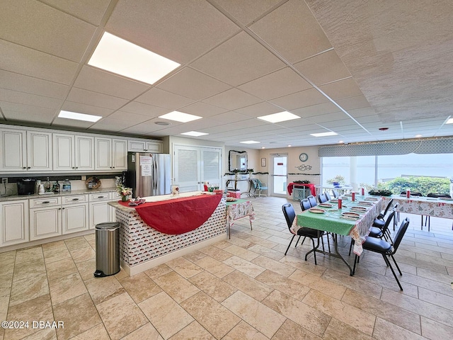 kitchen featuring stainless steel refrigerator, a drop ceiling, and white cabinets