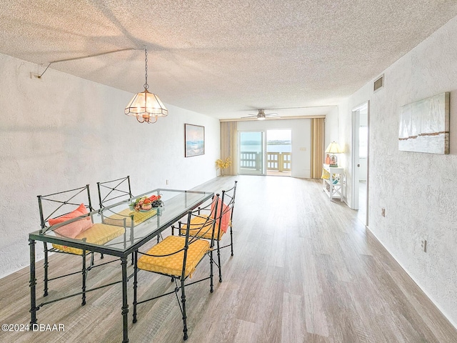 dining room featuring ceiling fan with notable chandelier, wood-type flooring, and a textured ceiling