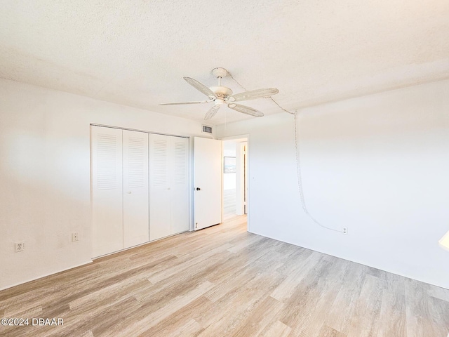 unfurnished bedroom with ceiling fan, a closet, a textured ceiling, and light hardwood / wood-style flooring