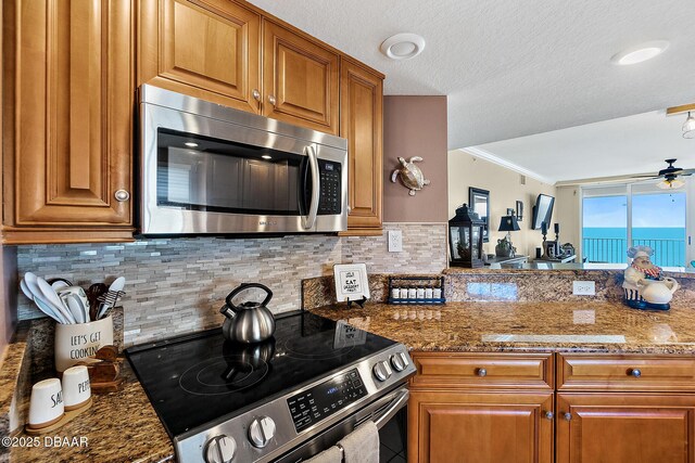 3145 S Atlantic Ave Unit 504, Daytona Beach Shores, FL 32118 - kitchen with appliances with stainless steel finishes, decorative backsplash, ceiling fan, brown cabinetry, and stone countertops