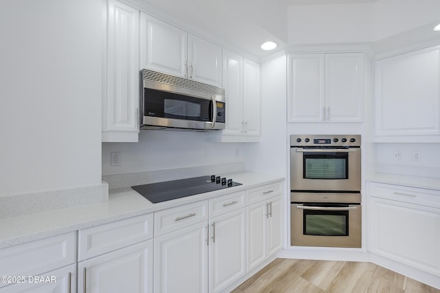 kitchen featuring light stone countertops, stainless steel appliances, white cabinets, and light wood-type flooring