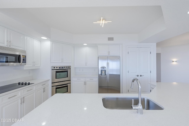 kitchen with white cabinetry, stainless steel appliances, sink, and light stone counters