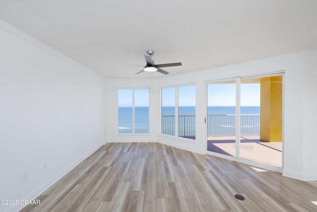 unfurnished room featuring a textured ceiling, light hardwood / wood-style floors, ceiling fan, and a water view