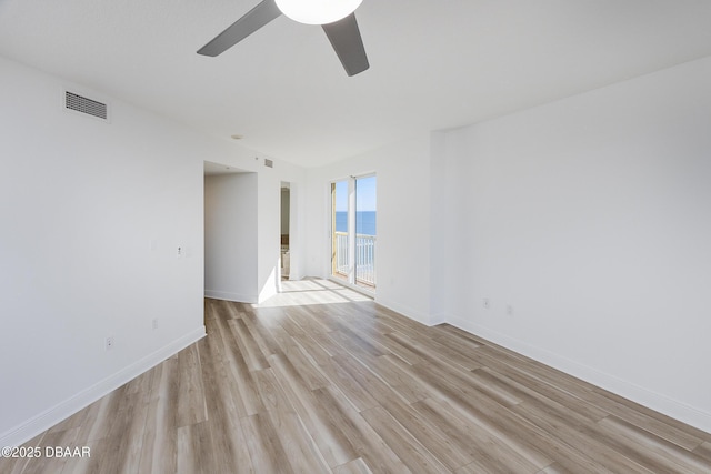 empty room featuring a water view, ceiling fan, and light wood-type flooring