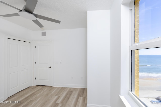 unfurnished bedroom with ceiling fan, a water view, a textured ceiling, a closet, and light wood-type flooring