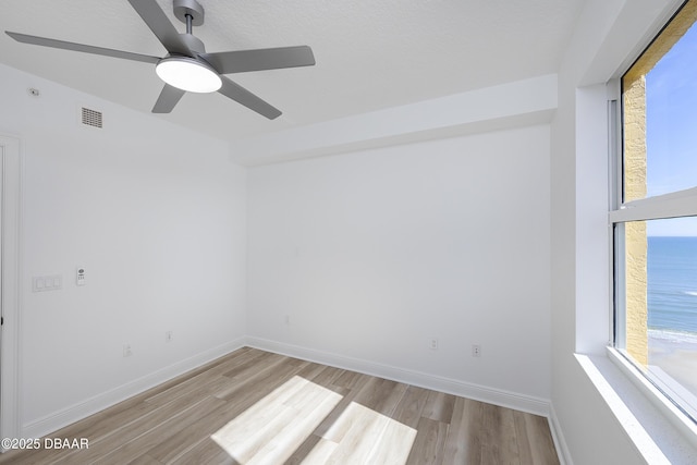 spare room with light hardwood / wood-style floors, ceiling fan, and a water view