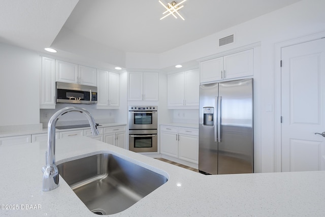 kitchen with white cabinetry, appliances with stainless steel finishes, light stone countertops, and sink