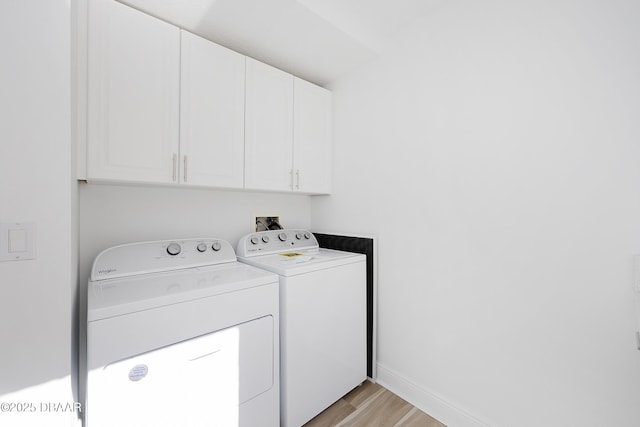 laundry room featuring cabinets, light wood-type flooring, and washer and clothes dryer