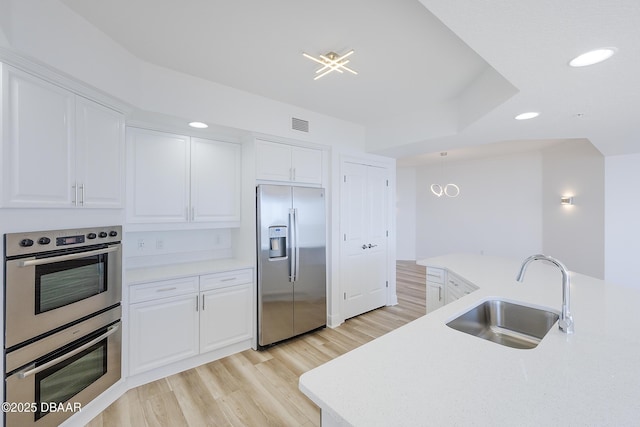 kitchen with white cabinetry, stainless steel appliances, decorative light fixtures, and sink