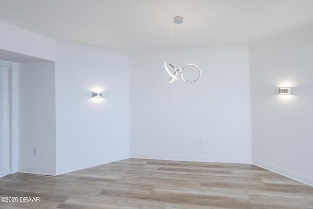 empty room with a notable chandelier, crown molding, and light hardwood / wood-style flooring