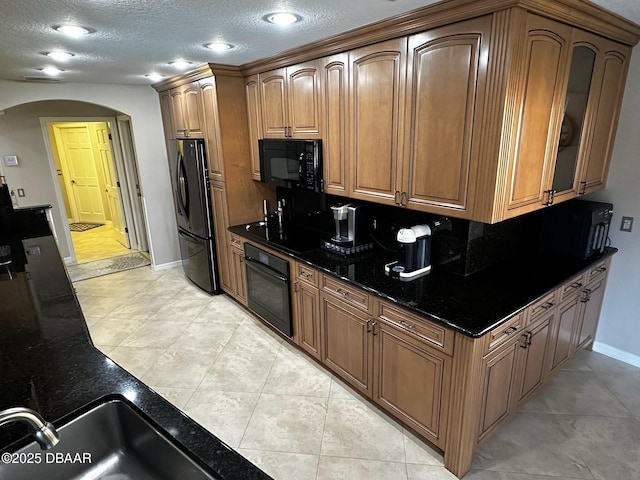 kitchen with a textured ceiling, light tile patterned floors, dark stone counters, decorative backsplash, and black appliances