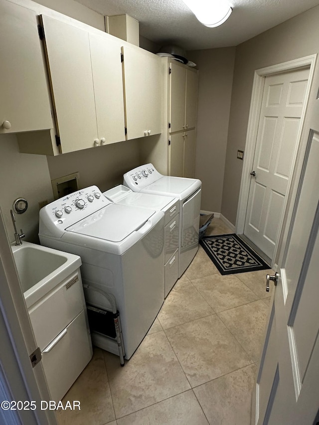 laundry room with light tile patterned floors, washer and clothes dryer, cabinets, and a textured ceiling