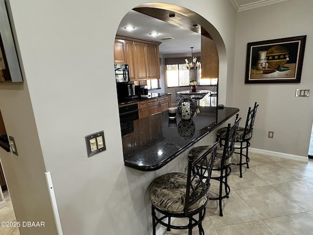 kitchen featuring decorative light fixtures, dark stone countertops, a kitchen breakfast bar, and black appliances