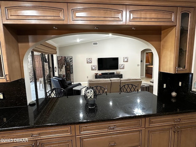 kitchen with tasteful backsplash, ornamental molding, lofted ceiling, and dark stone countertops