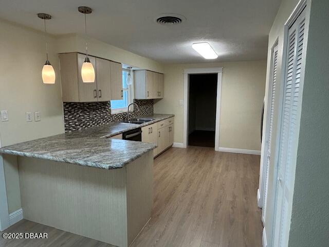 kitchen with decorative light fixtures, sink, kitchen peninsula, and light wood-type flooring