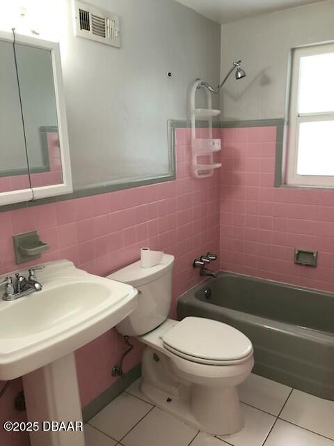 bathroom with toilet, tiled shower / bath combo, tile walls, and tile patterned floors