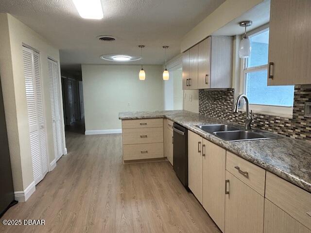 kitchen featuring pendant lighting, stainless steel dishwasher, kitchen peninsula, sink, and light brown cabinetry