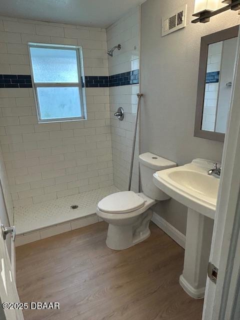 bathroom featuring toilet, a tile shower, and wood-type flooring