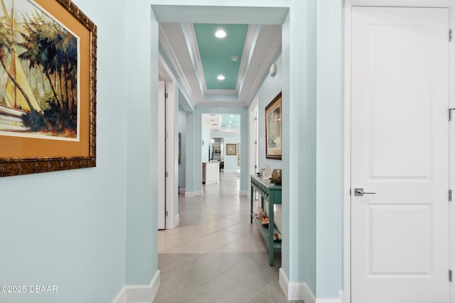 corridor featuring a tray ceiling, crown molding, and light tile patterned flooring