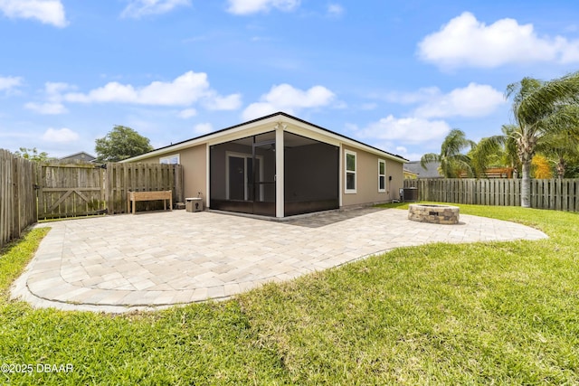 rear view of property featuring a patio, a fenced backyard, a sunroom, a lawn, and an outdoor fire pit