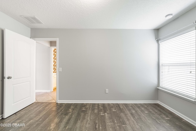 spare room featuring a healthy amount of sunlight, a textured ceiling, wood finished floors, and visible vents