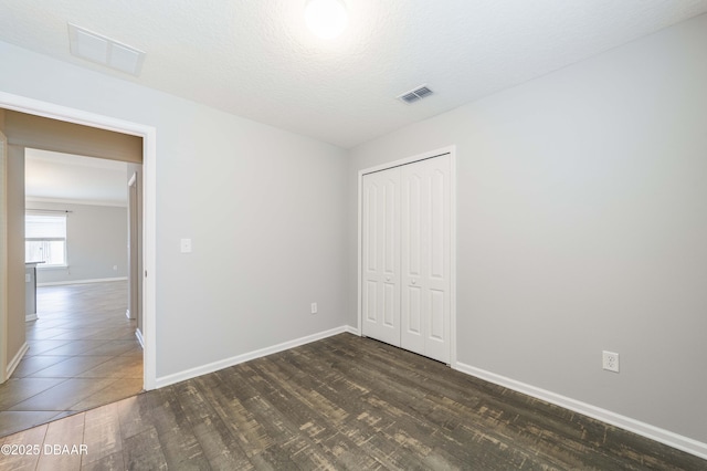unfurnished bedroom featuring a closet, baseboards, dark wood-type flooring, and visible vents