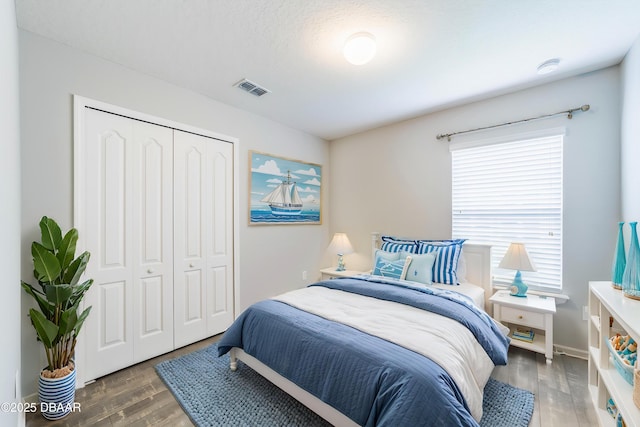 bedroom featuring baseboards, a closet, wood finished floors, and visible vents