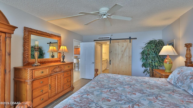 4139 S Atlantic Ave Unit A406, New Smyrna Beach, FL 32169 - bedroom with a barn door, a textured ceiling, wood finished floors, ceiling fan, and ensuite bath