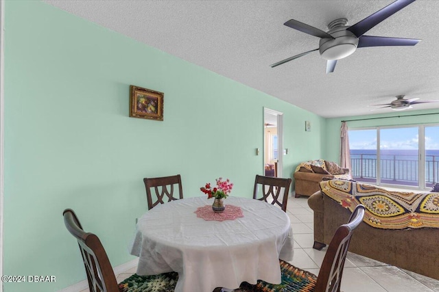 tiled dining space featuring ceiling fan, a textured ceiling, and a water view