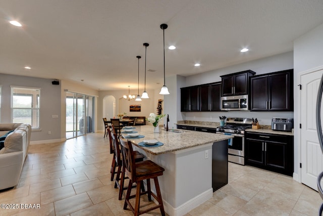 kitchen featuring arched walkways, open floor plan, stainless steel appliances, a kitchen bar, and a sink