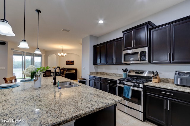 kitchen featuring an island with sink, light stone countertops, stainless steel appliances, pendant lighting, and a sink