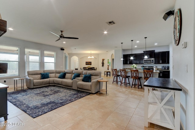 living area featuring arched walkways, light tile patterned floors, recessed lighting, ceiling fan with notable chandelier, and visible vents