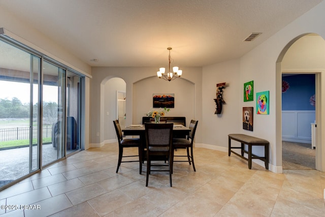 dining area featuring arched walkways, visible vents, a notable chandelier, and a textured ceiling