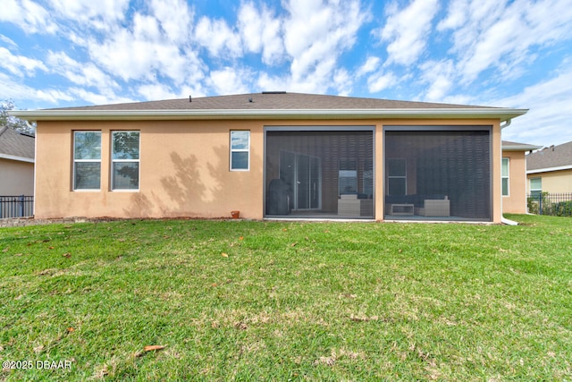 rear view of house featuring a yard, a sunroom, fence, and stucco siding