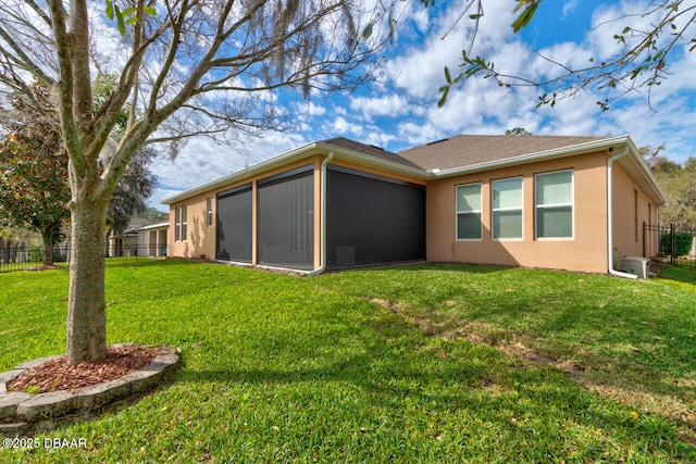 rear view of property featuring a yard, fence, a sunroom, and stucco siding