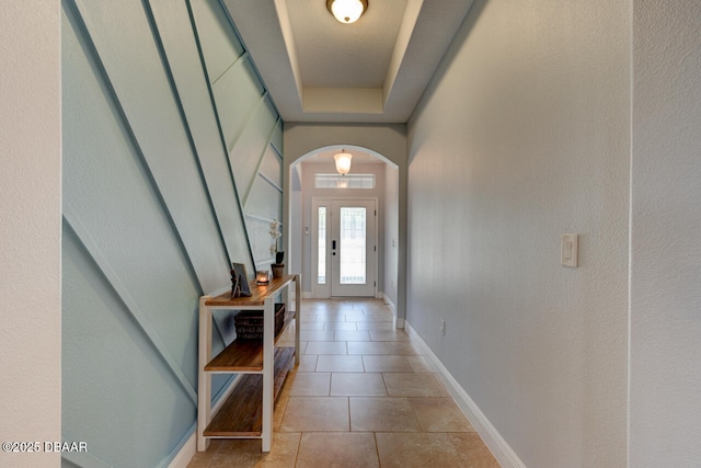 entryway featuring arched walkways, a raised ceiling, tile patterned floors, and baseboards