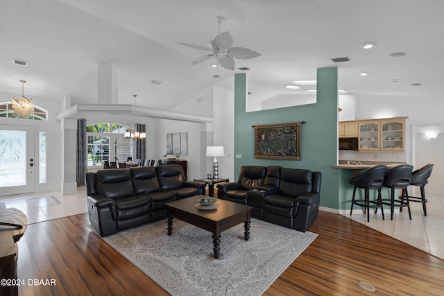 living room with ceiling fan with notable chandelier, light hardwood / wood-style floors, and vaulted ceiling