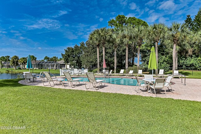 view of swimming pool featuring a lanai, a water view, a lawn, and a patio area