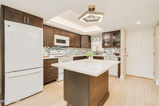 kitchen featuring white appliances, a tray ceiling, dark brown cabinetry, light countertops, and backsplash