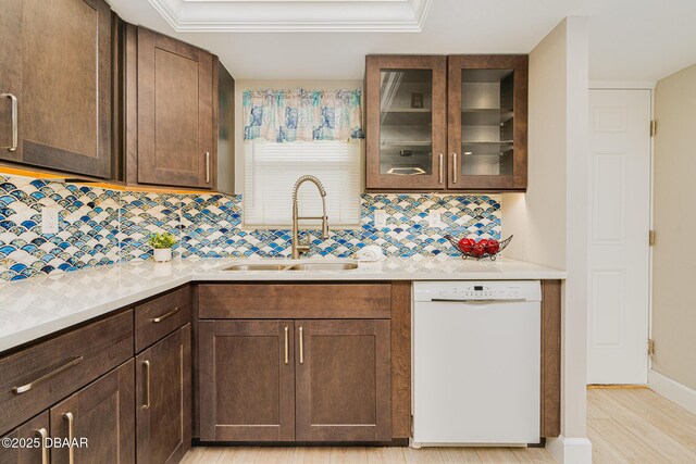 kitchen with white dishwasher, a sink, tasteful backsplash, and light countertops