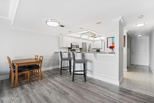 kitchen with kitchen peninsula, a breakfast bar area, appliances with stainless steel finishes, ornamental molding, and white cabinets