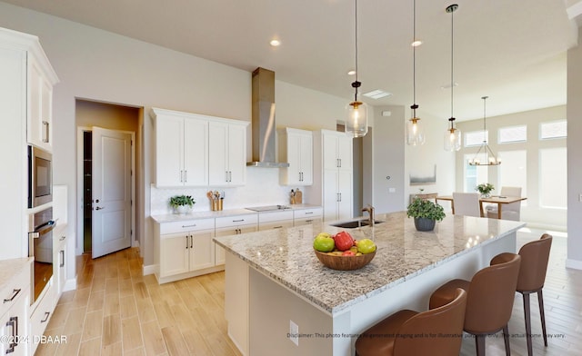 kitchen with a center island with sink, white cabinets, hanging light fixtures, wall chimney range hood, and appliances with stainless steel finishes