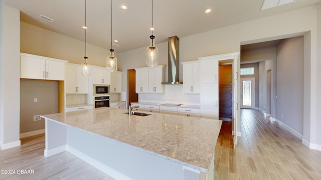 kitchen with white cabinetry, wall chimney exhaust hood, and a large island with sink