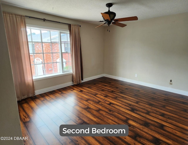 empty room featuring a ceiling fan, a textured ceiling, baseboards, and dark wood-type flooring