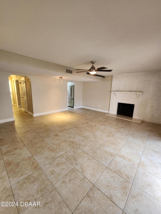 unfurnished living room with a brick fireplace, ceiling fan, light tile patterned floors, and visible vents