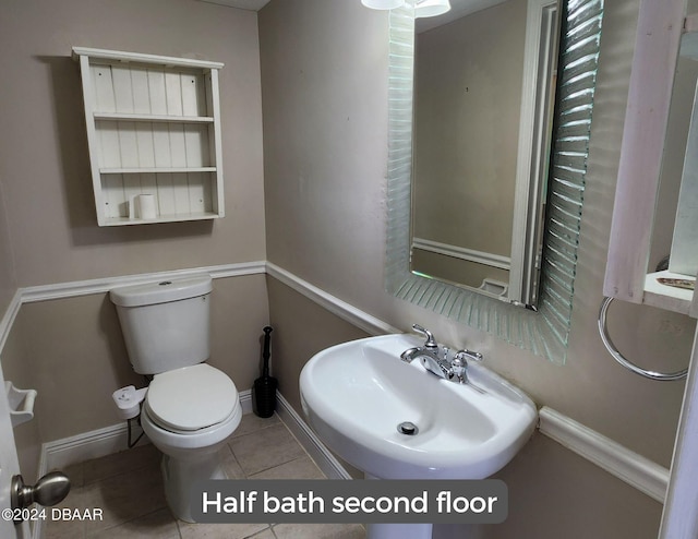 half bath with toilet, tile patterned flooring, baseboards, and a sink