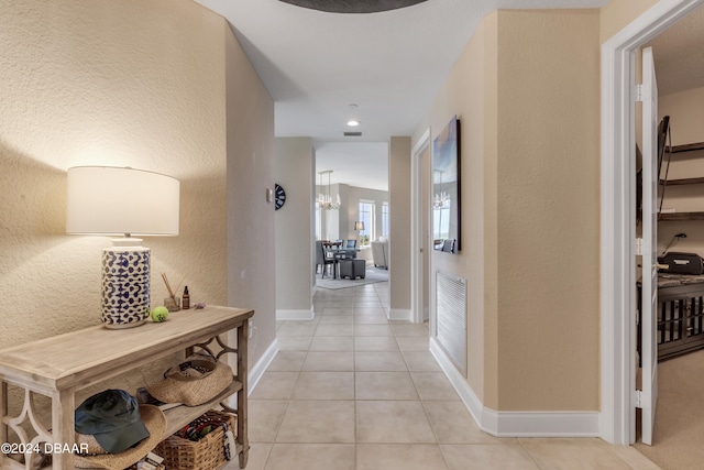 corridor with light tile patterned flooring and an inviting chandelier